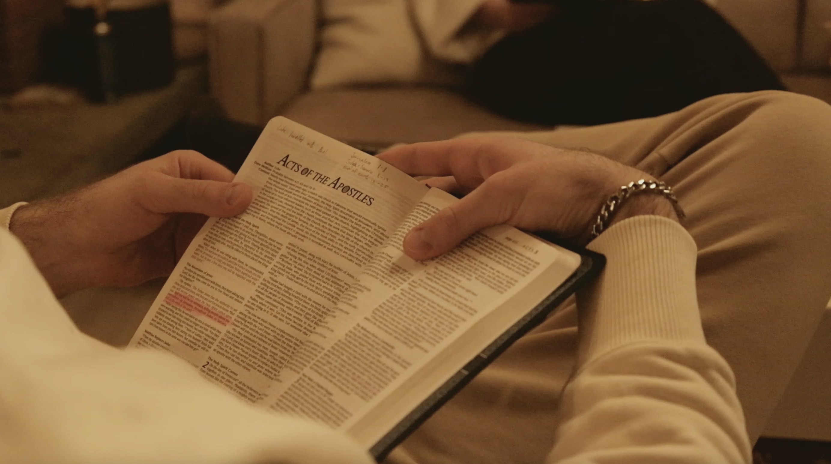 Hands holding an open Bible at the Acts of the Apostles, with handwritten notes